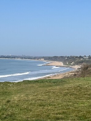 A coastal landscape with a grassy foreground, a sandy beach, and the ocean. - The Wing is a luxury and peaceful private retreat for two adults. (New Milton)