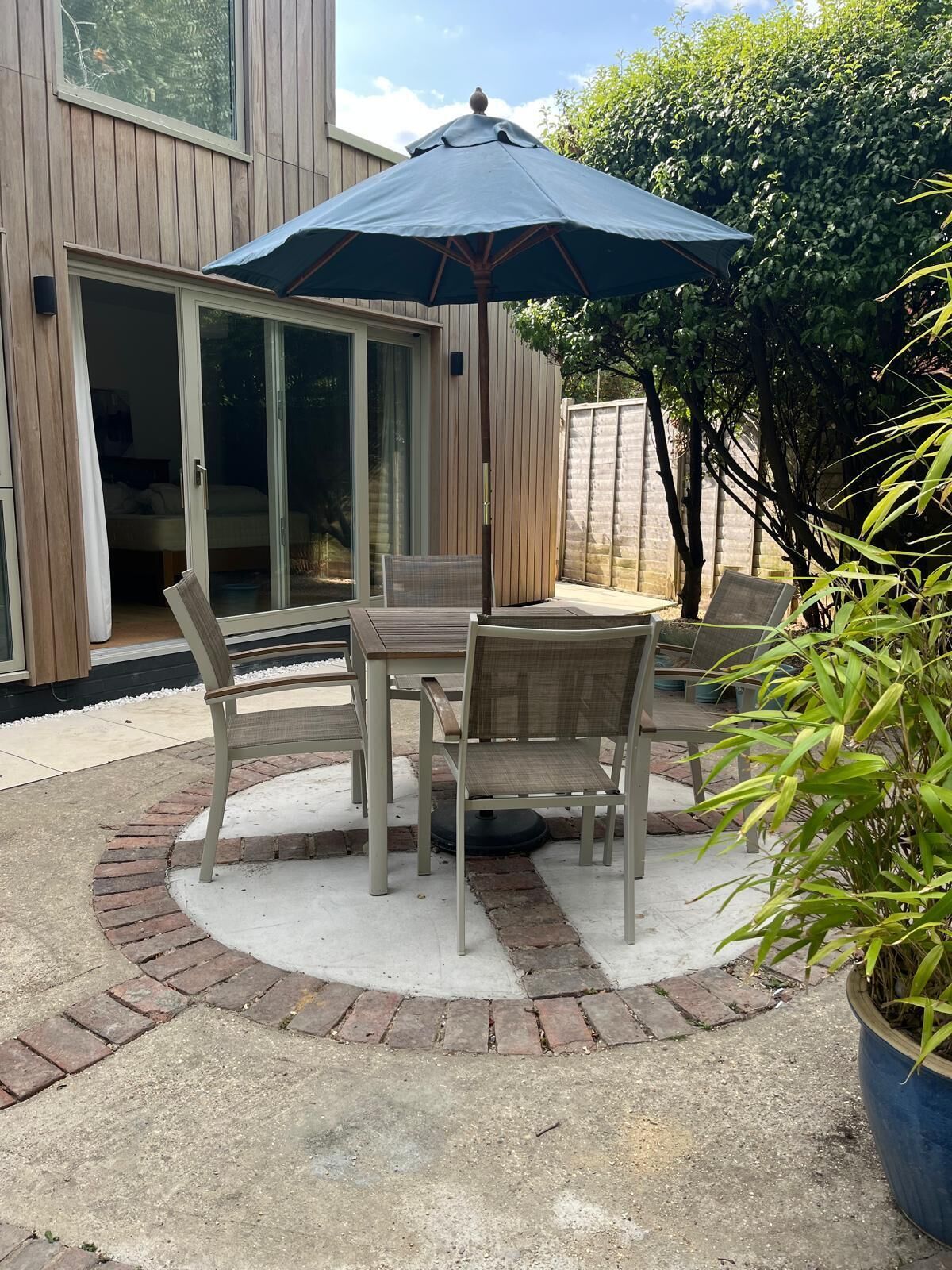An outdoor patio with a table and chairs, a large umbrella, and a potted plant.
