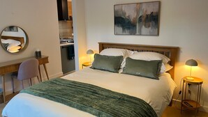 Ein Hotelzimmer mit einem Bett, Nachttischlampen, einem Schreibtisch, einem Sessel, einem Spiegel und einem Bild an der Wand.
