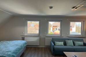 A modern room with a bed, a sofa, and a table. There are three windows providing views of the outside. - |---Harz Mountains---| (Sankt Andreasberg)