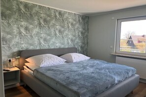 A bedroom with a bed, a nightstand, a window, and a wall with a leaf pattern. - |---Harz Mountains---| (Sankt Andreasberg)