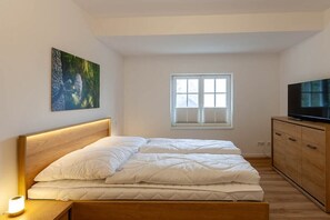 Une chambre à coucher avec un lit, une télévision, une fenêtre et un tableau au mur.