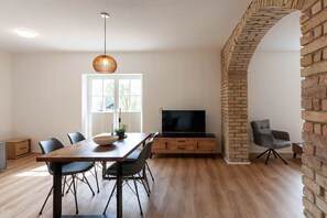 A modern living room with a wooden dining table, chairs, a TV, and a brick column. - Holiday apartment with 1 bedroom (Braunlage)