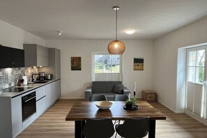 Eine moderne Küche mit Essbereich, ausgestattet mit einem Holztisch, einem grauen Sofa und einer Pendelleuchte.