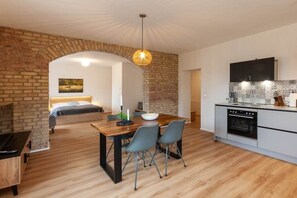 A modern kitchen with a built-in oven, a dining area with a wooden table and chairs, and a brick wall archway leading to a bedroom. - Holiday apartment with 1 bedroom (Braunlage)