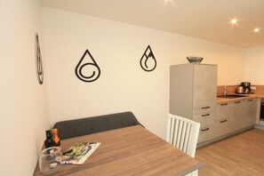 Een kleine keuken met een houten tafel, een witte stoel, een grijze kast en een kleine koelkast.