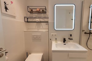 Une salle de bain moderne avec un lavabo blanc, un miroir avec éclairage intégré et une douche.