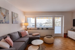 Un salon avec un canapé gris, une petite table ronde et une fenêtre donnant sur un paysage enneigé.