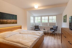 Une chambre à coucher avec un lit, deux chaises, une petite table, un téléviseur et un tableau accroché au mur.