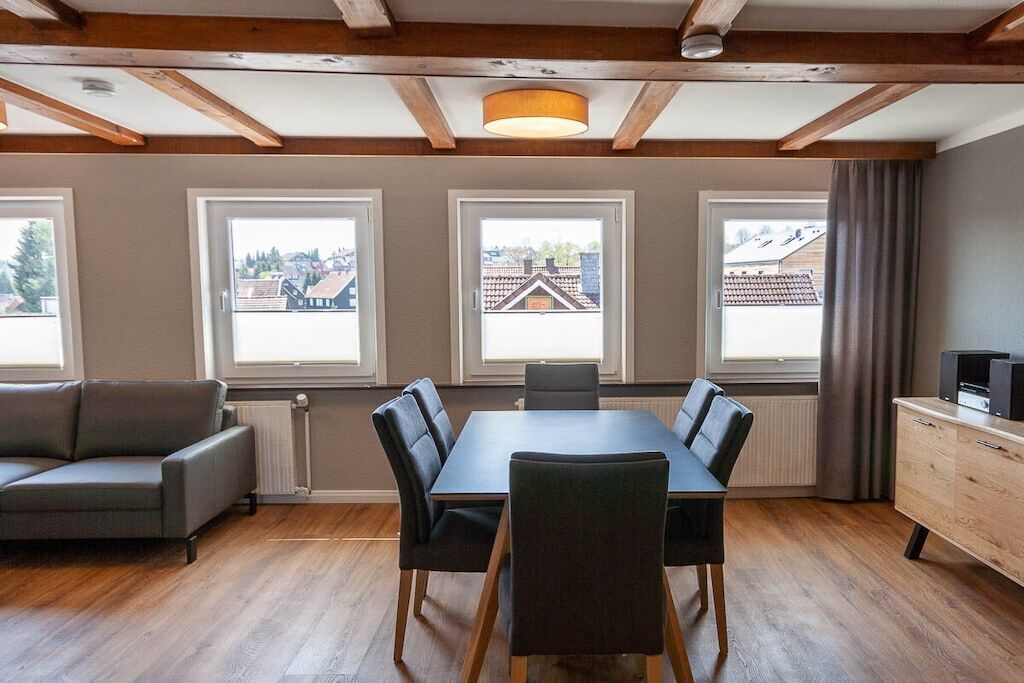 A dining area with a table and chairs, large windows with views, a sofa, and a cabinet.