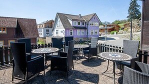 Uma área externa com mesas e cadeiras redondas, vista para casas coloridas e um céu limpo.