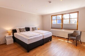 Une chambre avec deux lits, une chaise, une fenêtre et un radiateur.