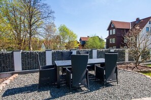 Un espace extérieur aménagé avec une table et des chaises, entouré d’une clôture en métal et recouvert de gravier.