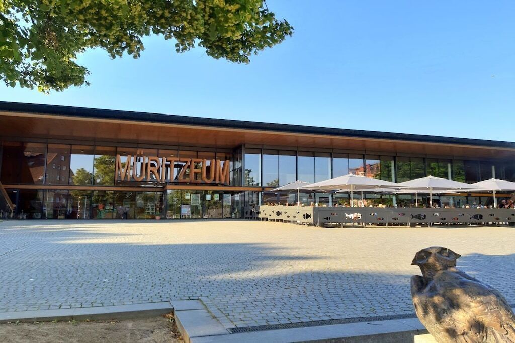 A modern building with a sign reading 'MUTIZEEUM' and a seating area with umbrellas.