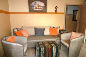 Ein Wohnzimmer mit einer Couch, zwei Sesseln, einem Couchtisch und einem Gemälde an der Wand.