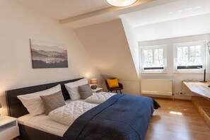 Ein Schlafzimmer mit einem Bett, Nachttischen, einem Sessel, einem Schreibtisch und einem Fenster.