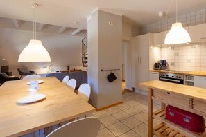 Eine moderne Küche mit Holztisch und -stühlen, einer Pendelleuchte und einer gefliesten Rückwand.