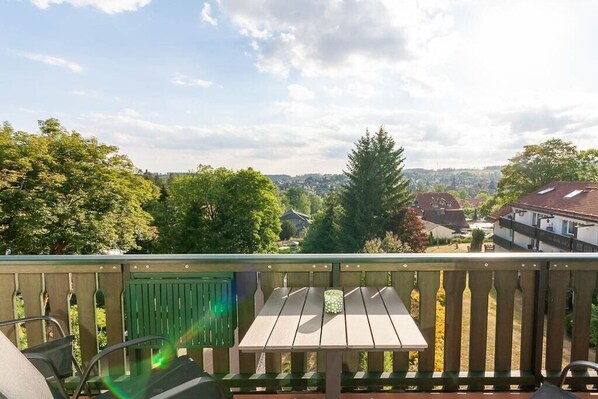 A balcony with a table and chairs, overlooking a residential area with houses and trees. - Eye-catching with a dream view (Braunlage)