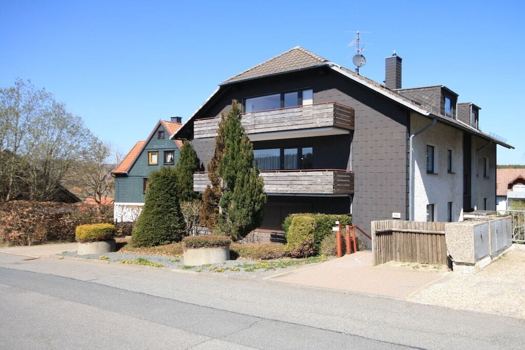 A two-story residential building with a sloped roof, a balcony on the upper floor, and a chimney.