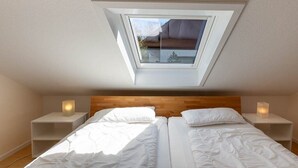 Quarto com claraboia, duas camas, cabeceira de madeira, mesas de cabeceira com velas e vista para o exterior.