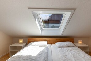 Une chambre avec un puits de lumière, deux lits, une tête de lit en bois, des tables de chevet avec des bougies et une vue sur l’extérieur.
