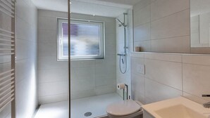 Casa de banho moderna com chuveiro envidraçado, sanita e lavatório.