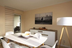 A dining area with a white table and chairs, a cabinet with decorative items, and a painting of a deer on the wall. - Holiday apartment with 2 bedrooms (Braunlage)