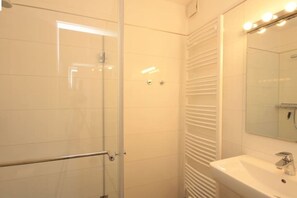 A bathroom with a glass shower enclosure, a white sink, and a mirror with lights above it. - Holiday apartment with 2 bedrooms (Braunlage)