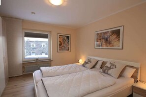 A bedroom with a large bed, a window with blinds, and two wall-mounted pictures. - Holiday apartment with 2 bedrooms (Braunlage)