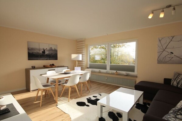 A modern living space with a dining area, a sofa, and a large window providing natural light. - Holiday apartment with 2 bedrooms (Braunlage)