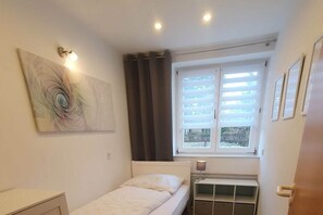 A small, single-bed room with a window, a radiator, and a wall-mounted light fixture. - Brocken summit with terrace (Schierke)