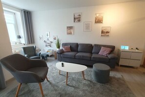 A modern living room with a grey sofa, a round coffee table, a grey armchair, and a small grey ottoman. - Brocken summit with terrace (Schierke)