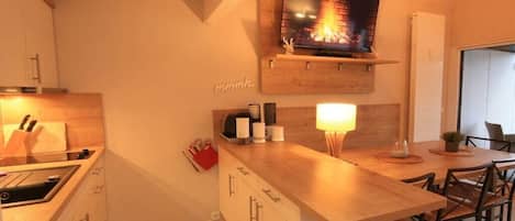 A modern kitchen with a built-in stove, wooden cabinets, a dining area with a wooden table and chairs, and a mounted television above the stove.