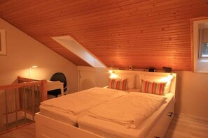 Une chambre avec un plafond en pente, un lit avec une literie blanche et un petit bureau avec une chaise.