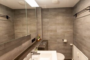 Ein modernes Badezimmer mit einem großen Spiegel, einem weißen Waschbecken und einer Toilette.
