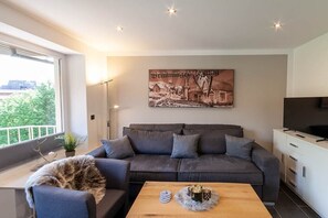 Ein modernes Wohnzimmer mit einem grauen Sofa, einem Holztisch und einem Stadtbild an der Wand.