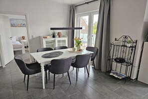 A modern dining area with a white table, grey chairs, and a black pendant light. - Holiday apartment with 3 bedrooms (Dangast)