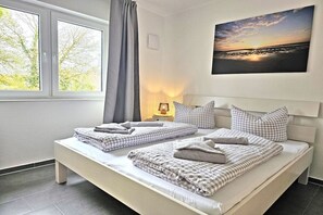 A bedroom with two beds, a window with curtains, a wall-mounted painting, and a bedside table with a lamp. - Holiday apartment with 3 bedrooms (Dangast)