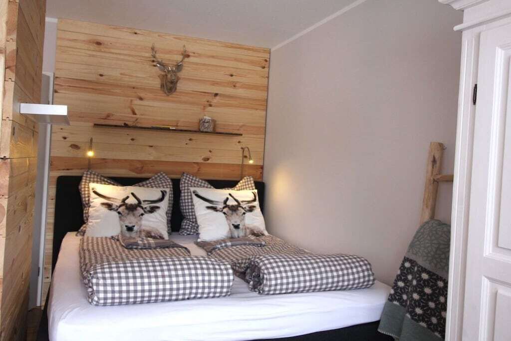 Un dormitorio con cabecera de madera, una cama con ropa de cama a cuadros y un ciervo montado en la pared.