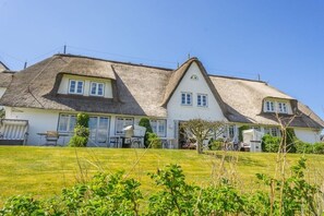 Ein zweistöckiges Haus mit einem Strohdach, einer Rasenfläche und einem kleinen Garten.