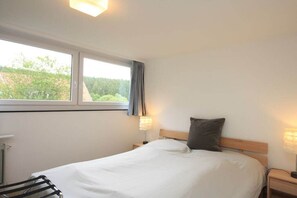 A bedroom with a bed, a nightstand, a lamp, a window, and a view of greenery outside. - Holiday apartment with 3 bedrooms (Braunlage)