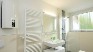 Casa de banho moderna com cabine de duche em vidro, lavatório branco com espelho e porta-toalhas.