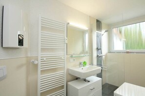 A modern bathroom with a glass shower enclosure, a white sink with a mirror, and a towel rack. - Holiday apartment with 3 bedrooms (Braunlage)