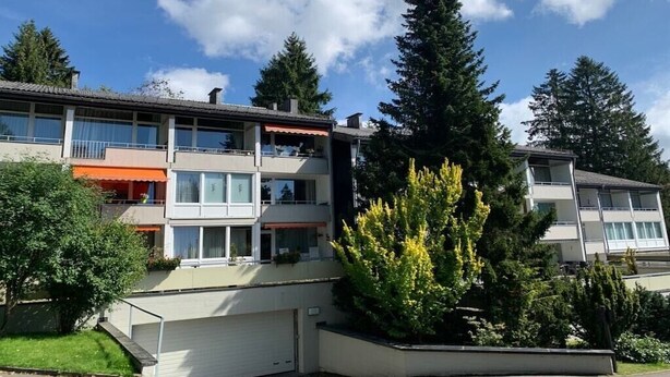 Um edifício residencial com vários andares, varandas, garagem e um jardim bem cuidado.