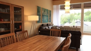 Uma sala de jantar com mesa e cadeiras de madeira, um armário com portas de vidro, um abajur e um sofá.