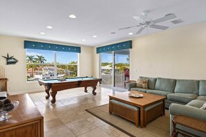 Un salon avec une table de billard, un canapé et une vue sur une piscine et des palmiers.