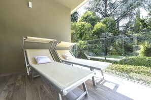 Ein Balkon mit zwei Sonnenliegen, einer Glasreling und Blick auf Grünflächen.