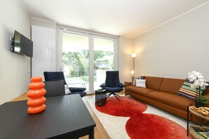 Ein modernes Wohnzimmer mit Flachbildfernseher, einer Couch, einem Esstisch und einem roten Teppich.