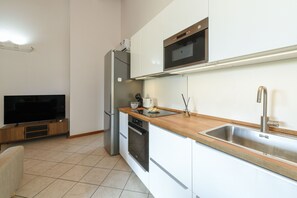 A modern kitchen with white cabinets, a stainless steel sink, a built-in oven, and a flat-screen TV. - MGH - Tavaredo Lake Retreat, Polpenazze (Polpenazze del Garda)