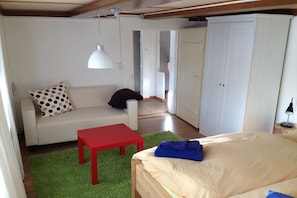 A small, compact room with a bed, a red table, a sofa with a polka dot pillow, and a white wardrobe. - Holiday apartment with 1 bedroom (Kleines Wiesental - Neuenweg)